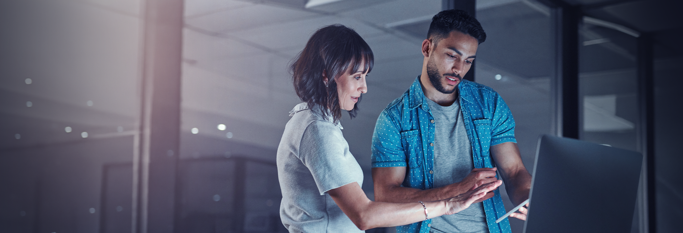 Two people looking at a computer and tablet in the office