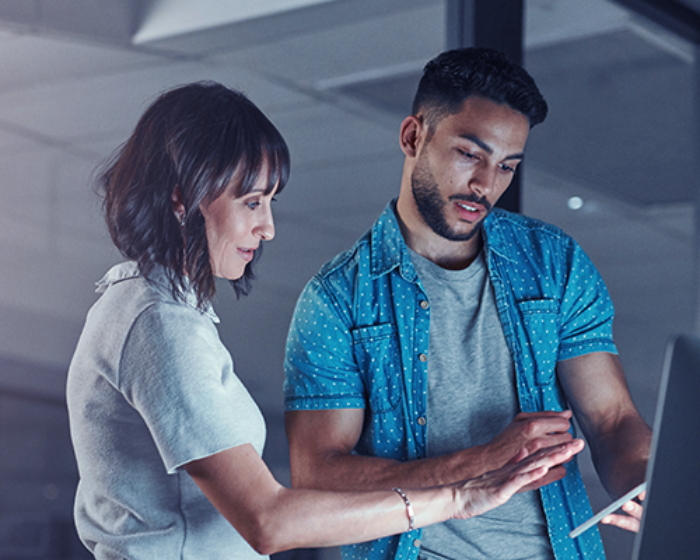 Two people looking at a computer and tablet in the office