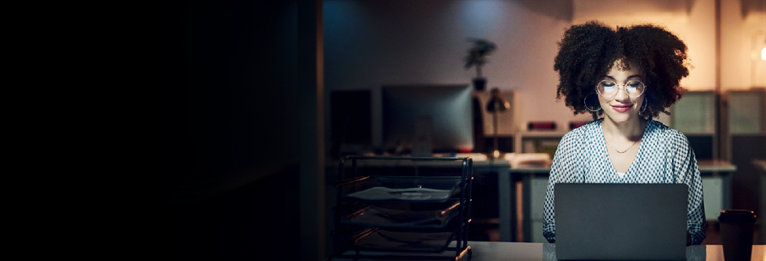 Woman working on a laptop at a desk in a softly lit office