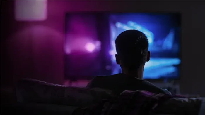 A view from behind of a person in a dark room watching a TV